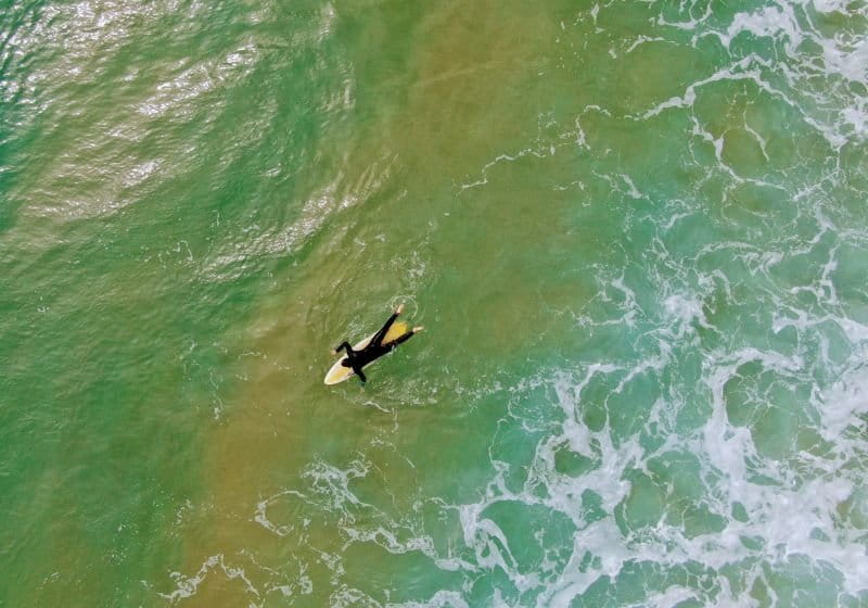 homem na praia deitado em uma prancha remando com as mãos