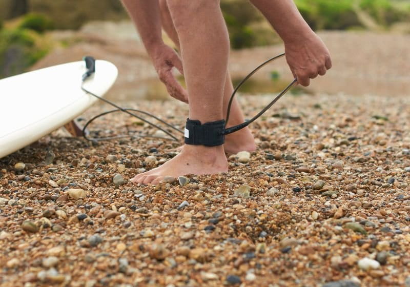 colocando Leash pessoa colocando Leash no pé e uma prancha ao lado