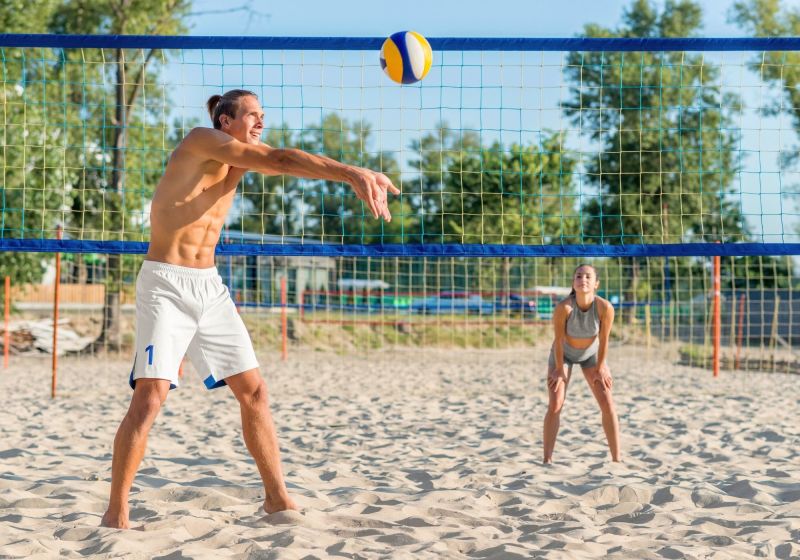 um homem e uma mulher jogando bolei em um quadra de areia