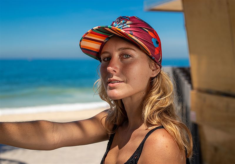 Mulher sentada, em praia, utilizando boné