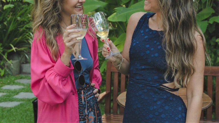 duas mulheres vestidas formalmente sorrindo e brindando com taças