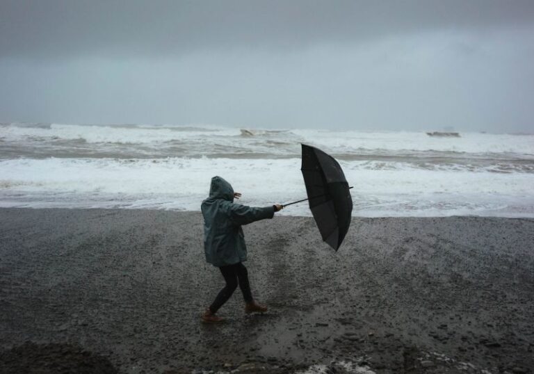 Um ser humano enfrentando a chuva na praia com um guarda chuvas