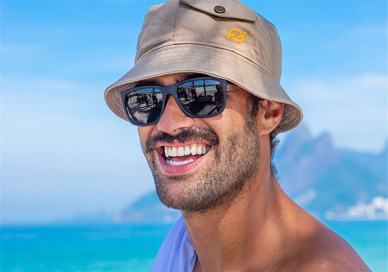 Rosto de homem sorridente utilizando chapéu e óculos de sol