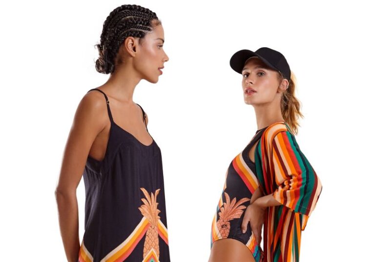 Duas mulheres, uma virada para a outra, uma utiliza vestido de alça e outra maio, quimono e boné