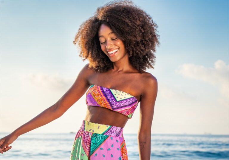 Mulher morena sorridente em praia com top e saia com estampa colorida