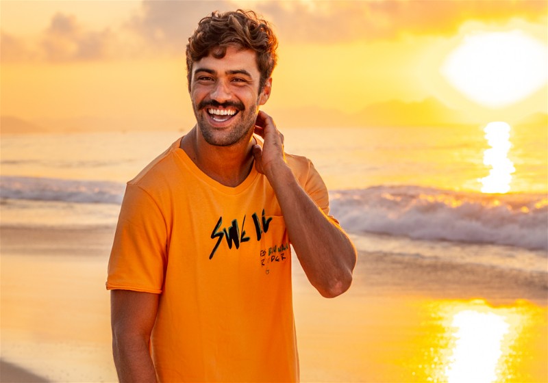 Homem sorridente em praia com mão no pescoço