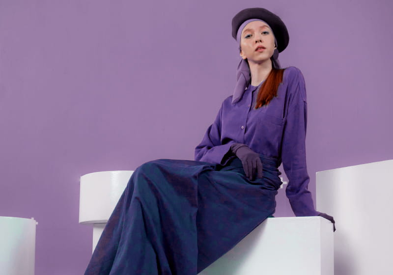 mulher ruiva sentada em um senário branco com fundo lilás com look todo monocromáticos da cor lilás 