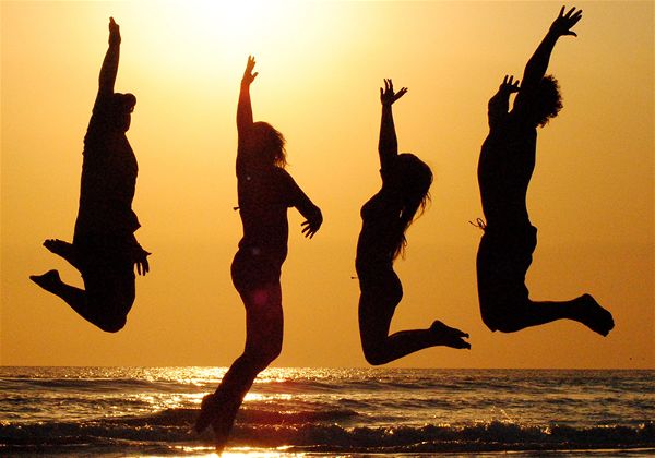 Silhueta de quatro pessoas pulando em frente ao mar com pôr do sol