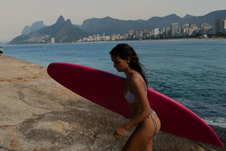 mulher segurando prancha de surfe e praia arpoador ao fundo
