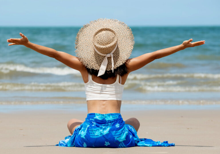 mulher sentada de costas com os braços abertos e mar ao fundo
